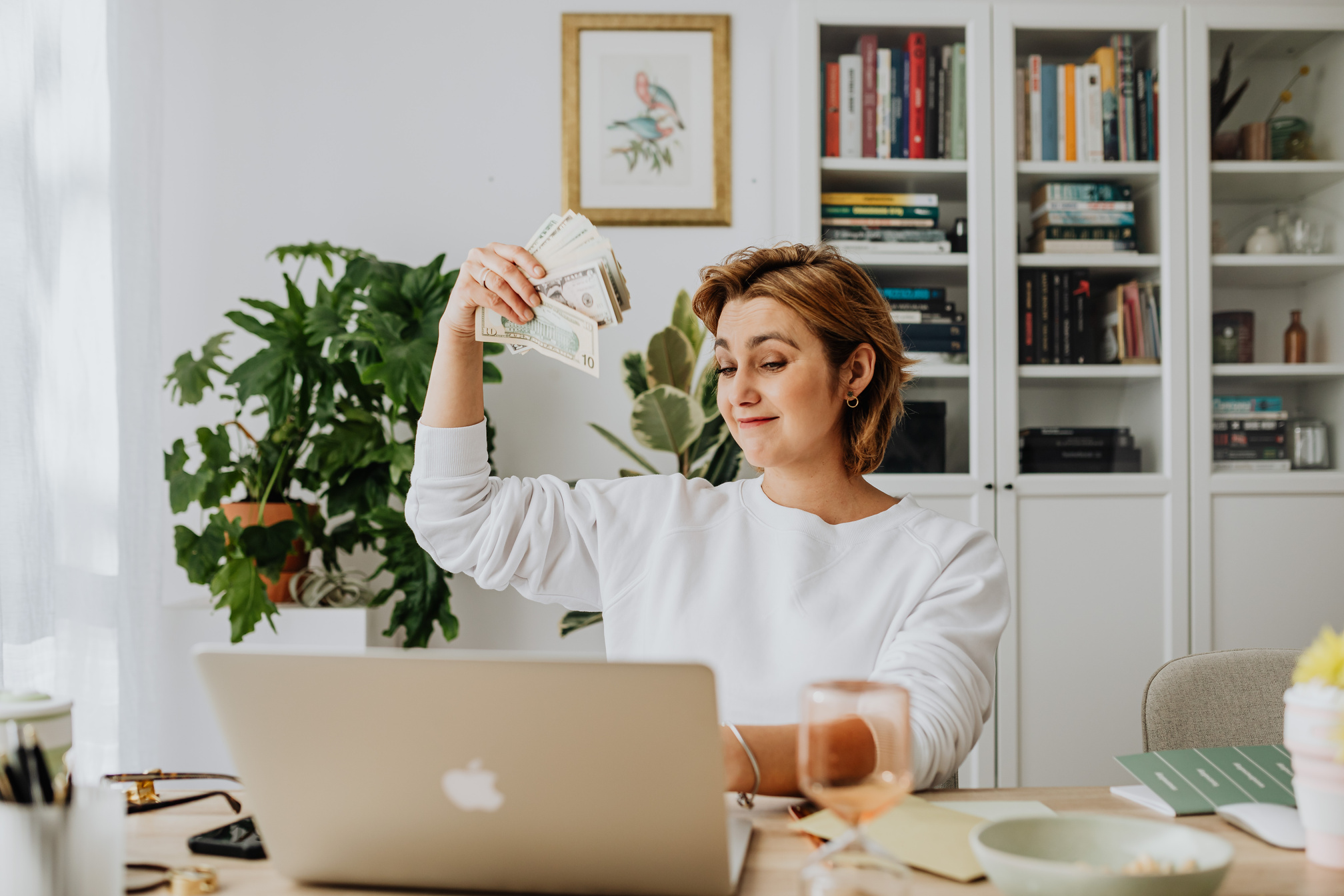 Woman Sitting in an Office in front of a Laptop and Waving Cash 